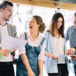 Four people smiling and looking at papers in colleague's hands.