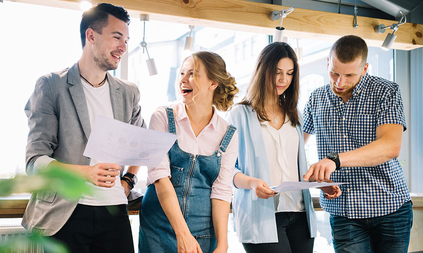 Four people smiling and looking at papers in colleague's hands.